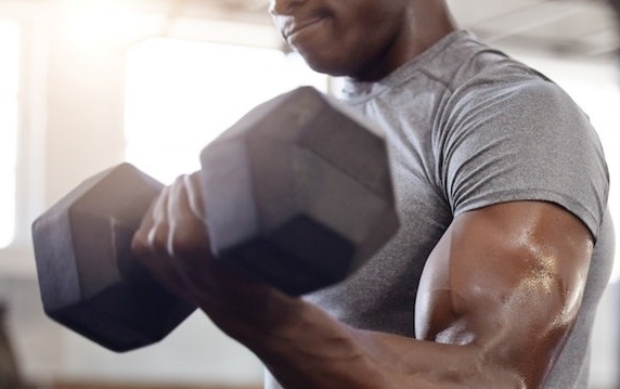 A black man strength training with dumbbells in the gym